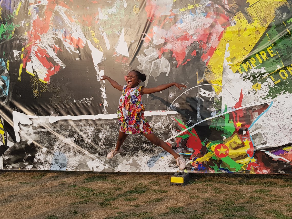 Young girl jumping in front of windrush mural